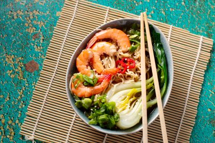 Ramen noodle soup with shrimp, green shallot, pak choi on green background