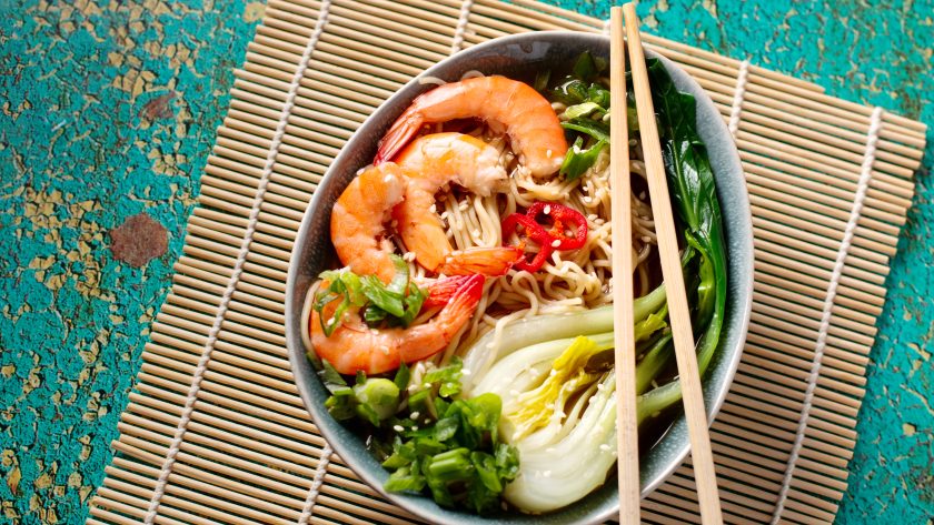 Ramen noodle soup with shrimp, green shallot, pak choi on green background